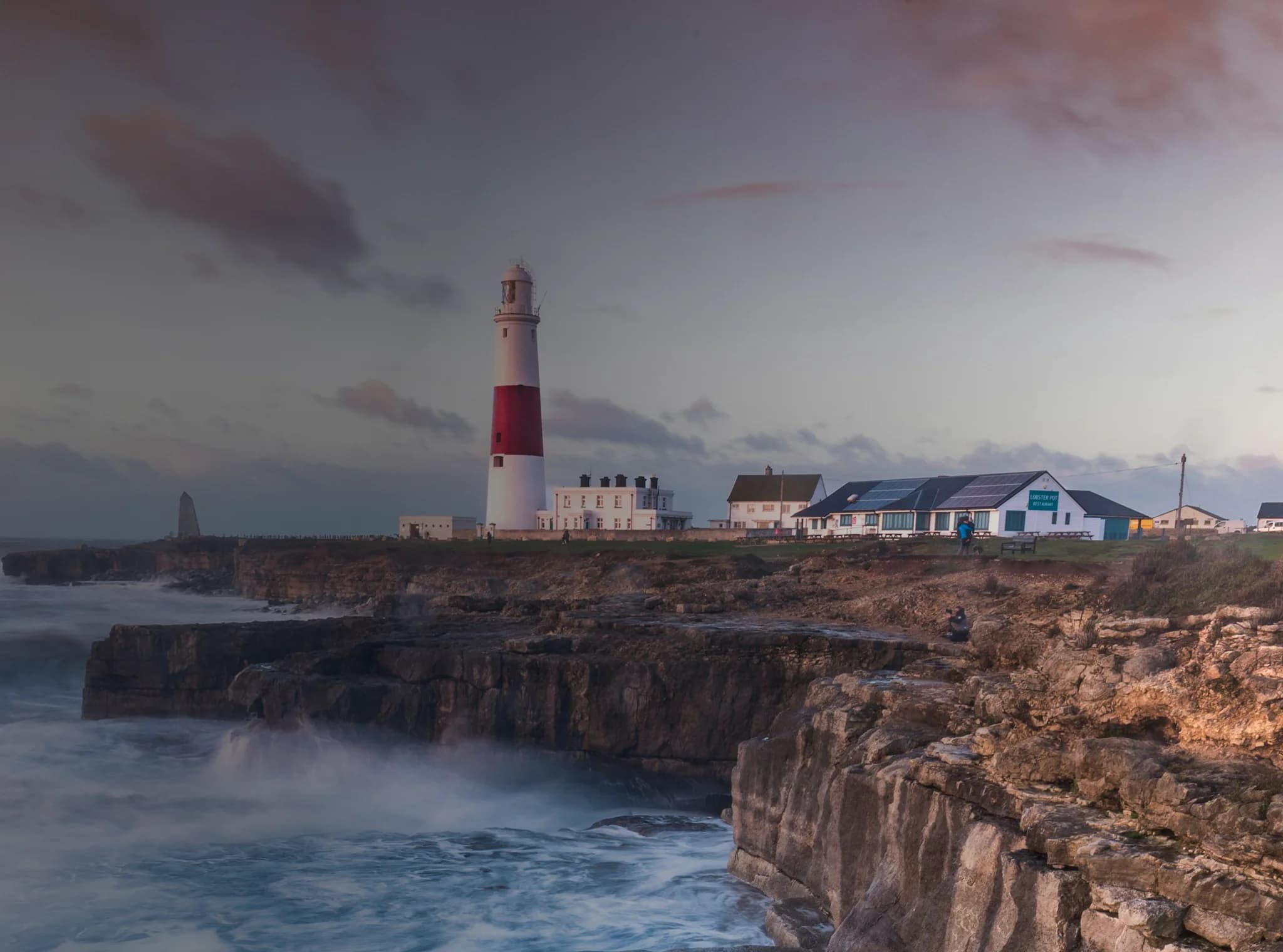 Wellen brechen auf einer britischen Klippe mit einem Leuchtturm in der Ferne