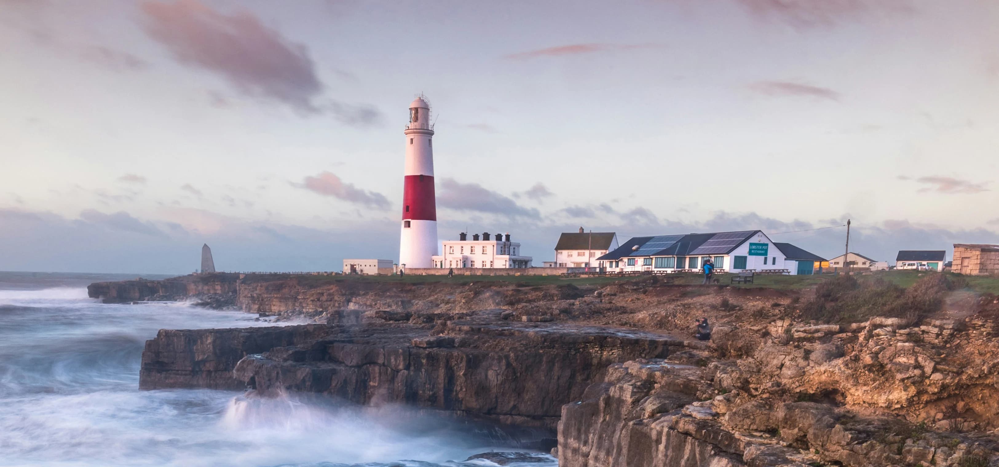 Wellen brechen auf einer britischen Klippe mit einem Leuchtturm in der Ferne