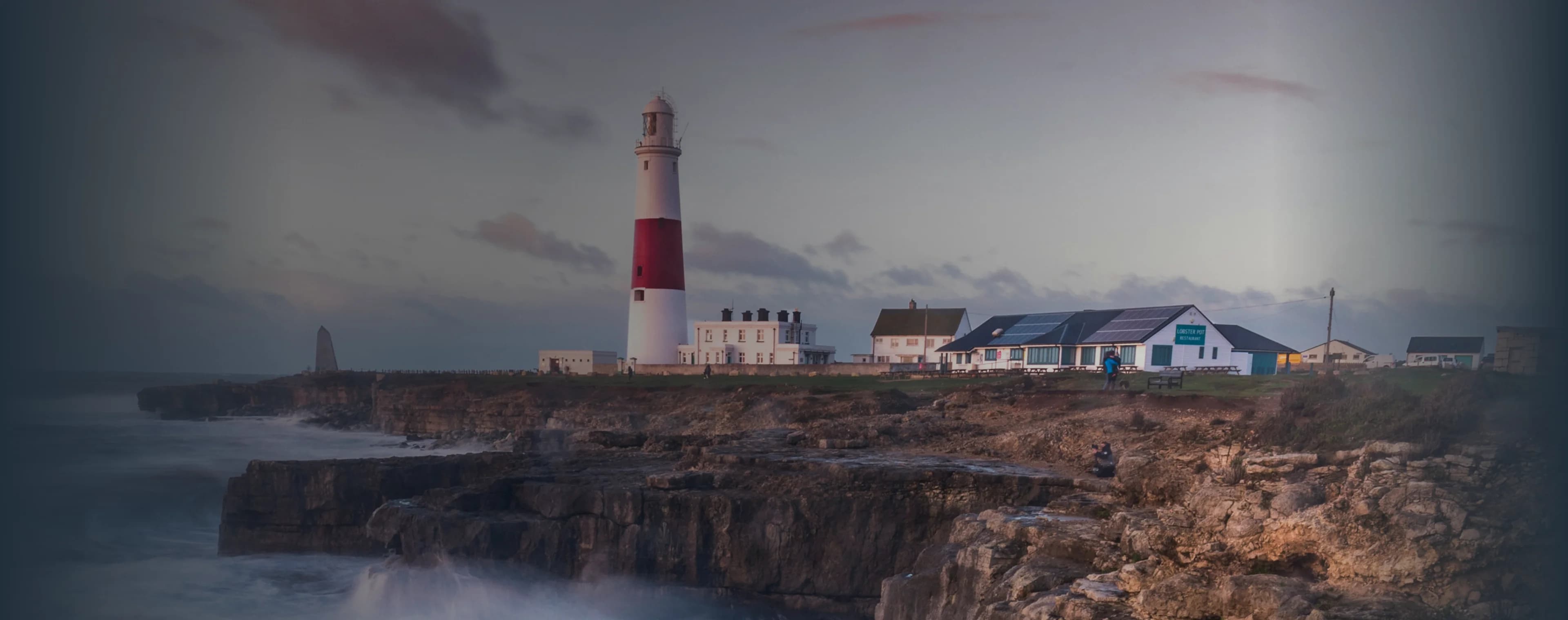 Wellen brechen auf einer britischen Klippe mit einem Leuchtturm in der Ferne
