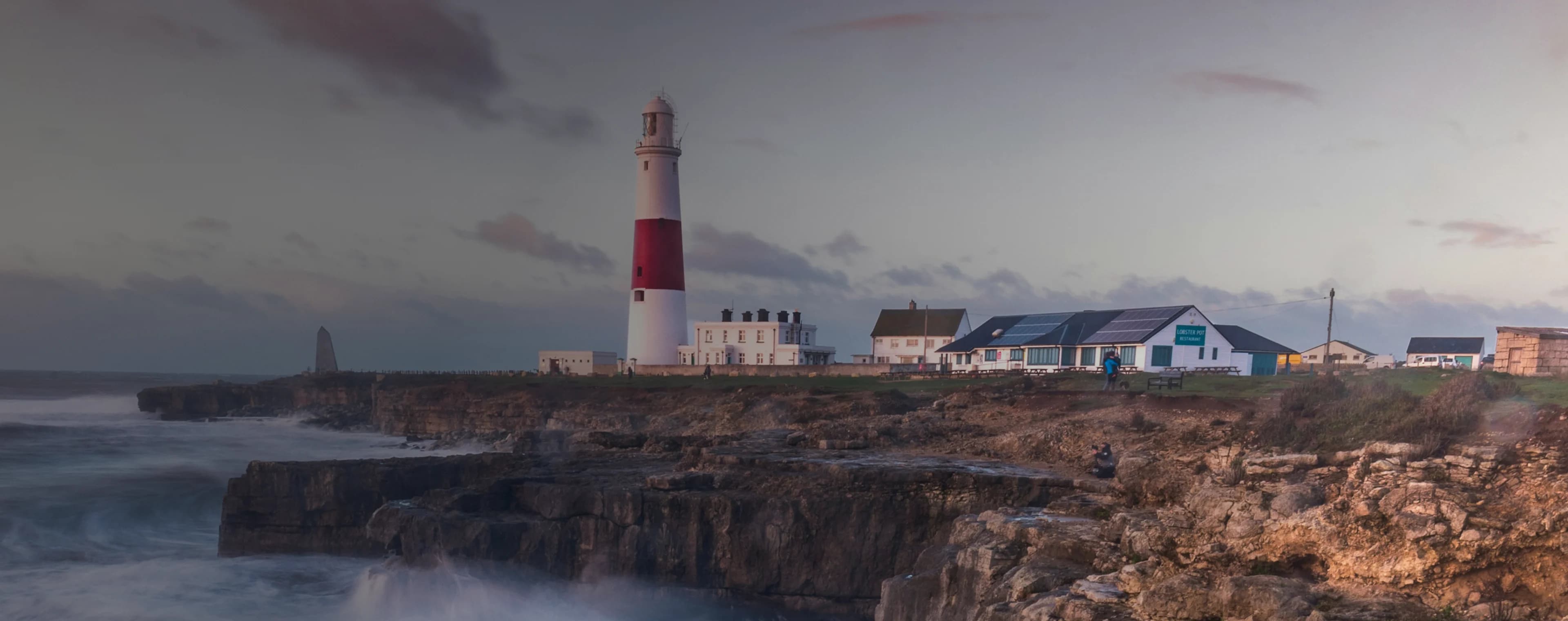 Wellen brechen auf einer britischen Klippe mit einem Leuchtturm in der Ferne
