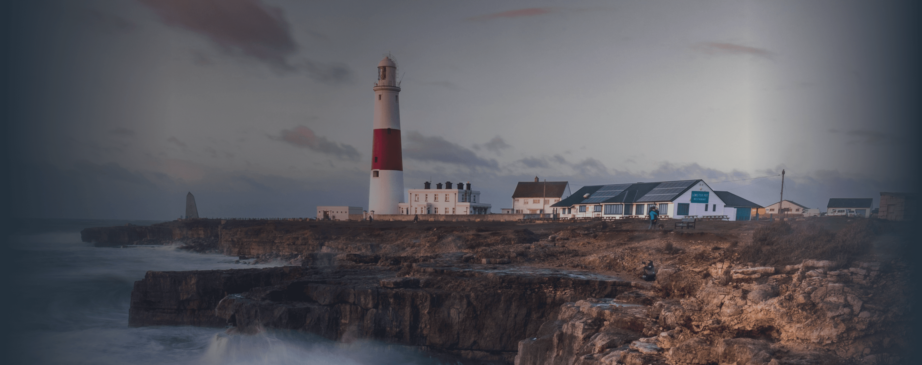 Wellen brechen auf einer britischen Klippe mit einem Leuchtturm in der Ferne