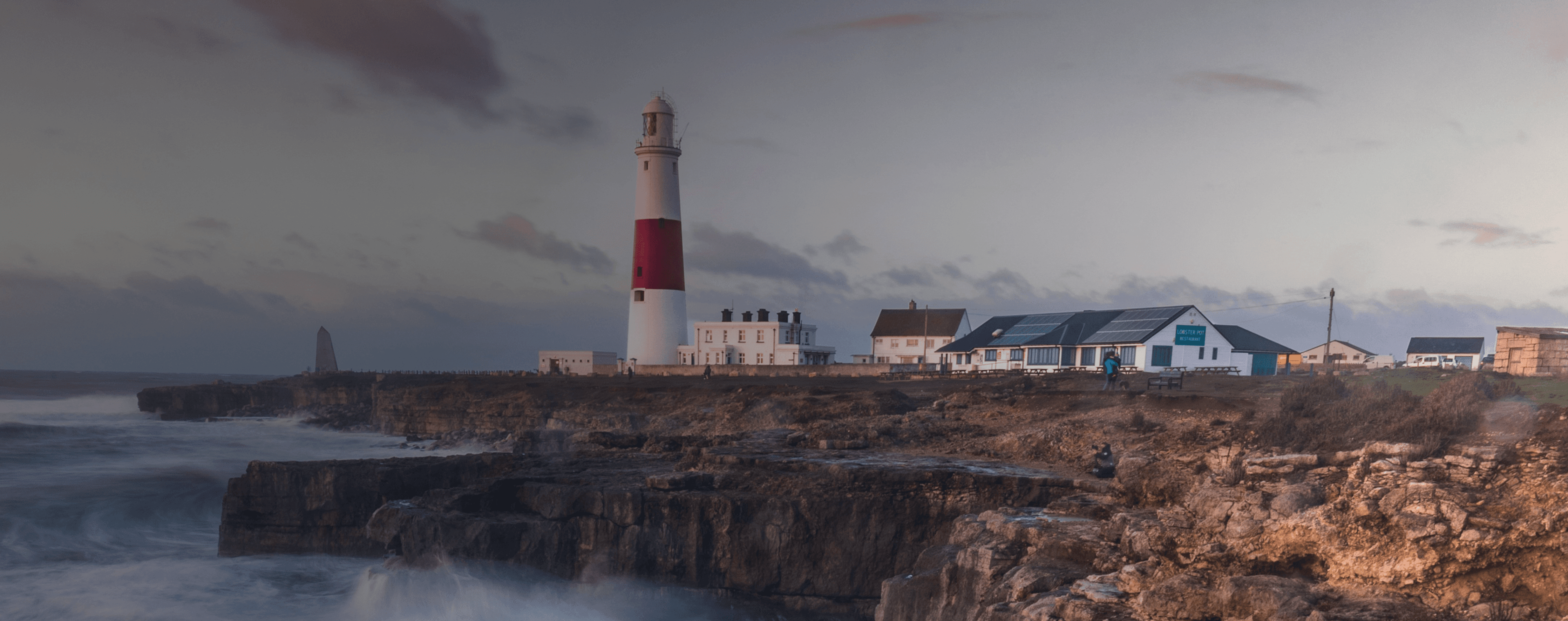 Wellen brechen auf einer britischen Klippe mit einem Leuchtturm in der Ferne