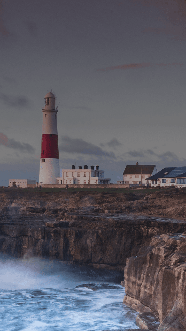 Wellen brechen auf einer britischen Klippe mit einem Leuchtturm in der Ferne