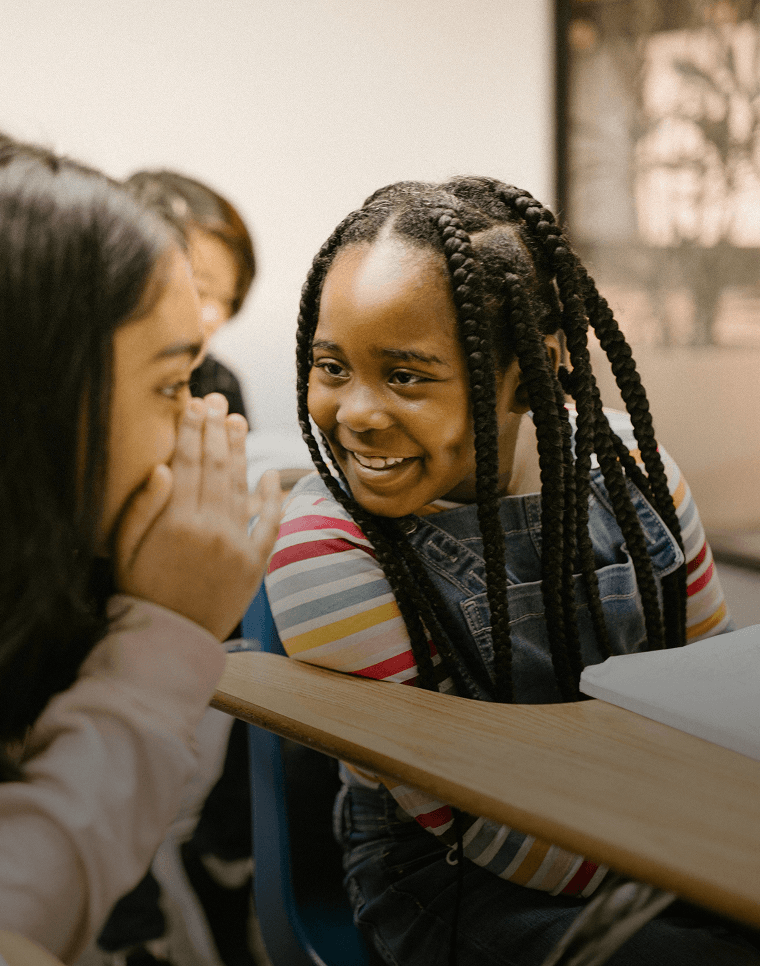 Lächelnde Schüler flüstern einander etwas zu, während sie in der Schule eine neue Sprache lernen.