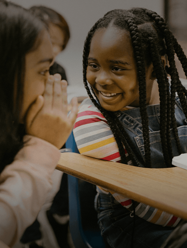 Lächelnde Schüler flüstern einander etwas zu, während sie in der Schule eine neue Sprache lernen.